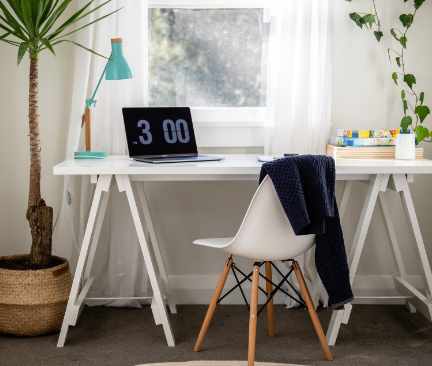 Wit bureau naast een plant in een kamer met een laptop