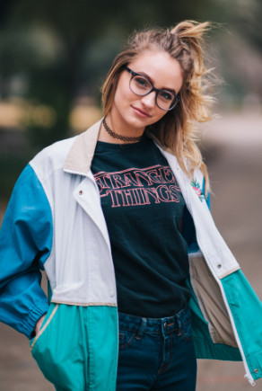 Jonge vrouw met een Stranger Things T-shirt, vintage harrington en tattooketting 