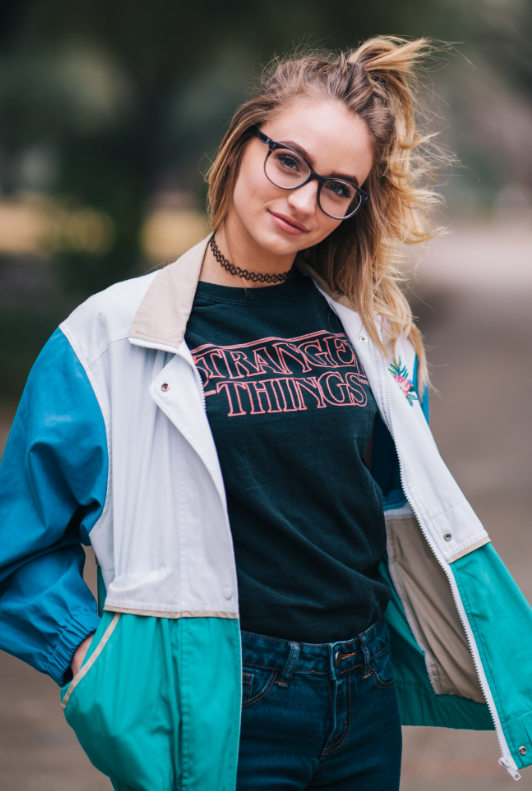 Modetrends 2020: Jonge vrouw met Stranger Things T-shirt, vintage blouson en tattooketting